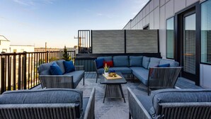 Un espace de détente extérieur moderne, composé d’un canapé d’angle, de deux fauteuils et d’une petite table, le tout disposé sur un tapis à motifs.