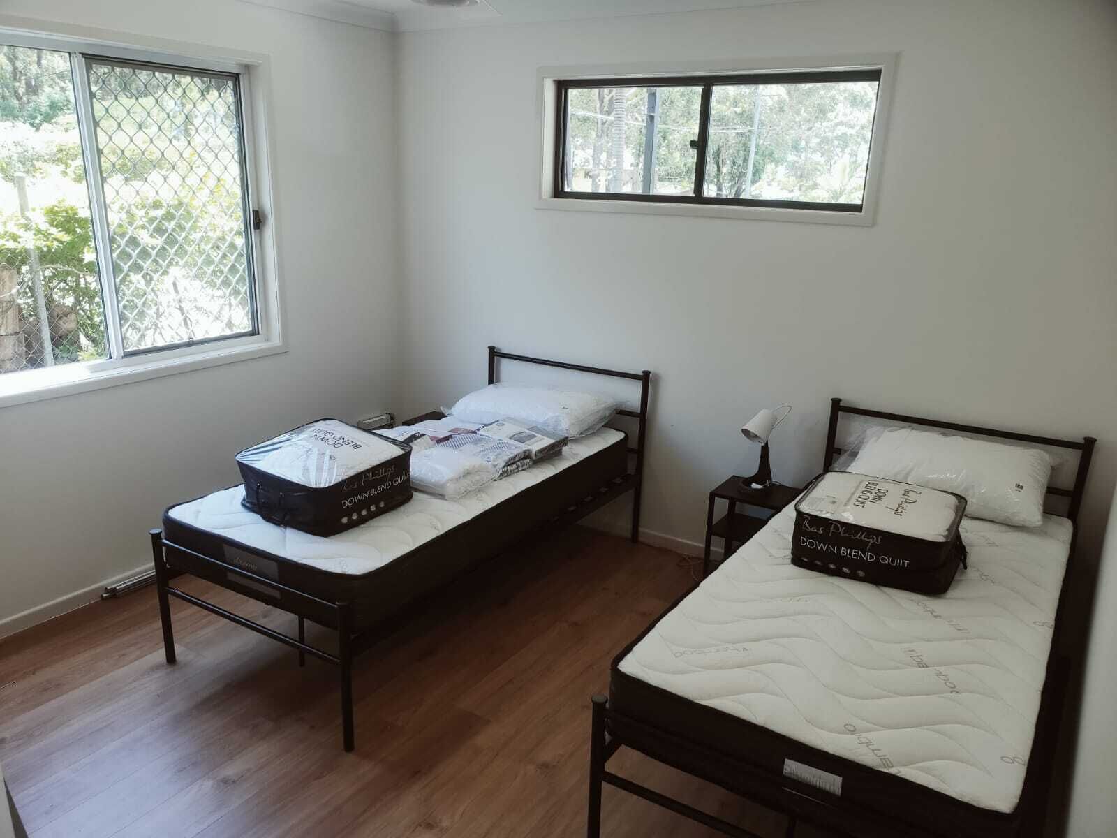 A bedroom with two single beds, a small table, a chair, and a window.