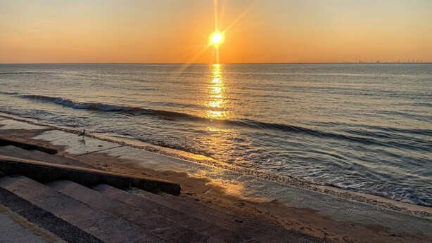 A sunset over a calm sea with a pier extending into the water.