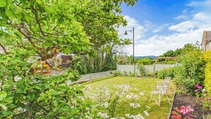 A well-maintained garden with a lawn, a white metal bench, and a variety of flowering plants.