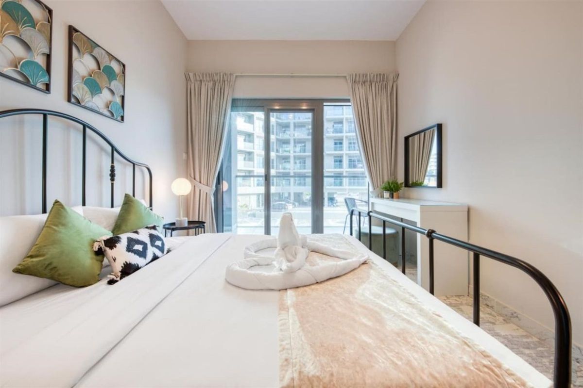 A hotel room with a bed, a desk, a window with curtains, and artwork on the wall.