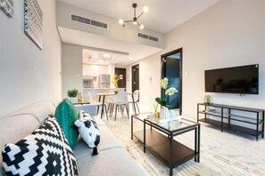 A modern living room with a sofa, coffee table, and a flat-screen TV mounted on the wall. - Stylish 1 BR + Pool & World Class Gym (Dubai)