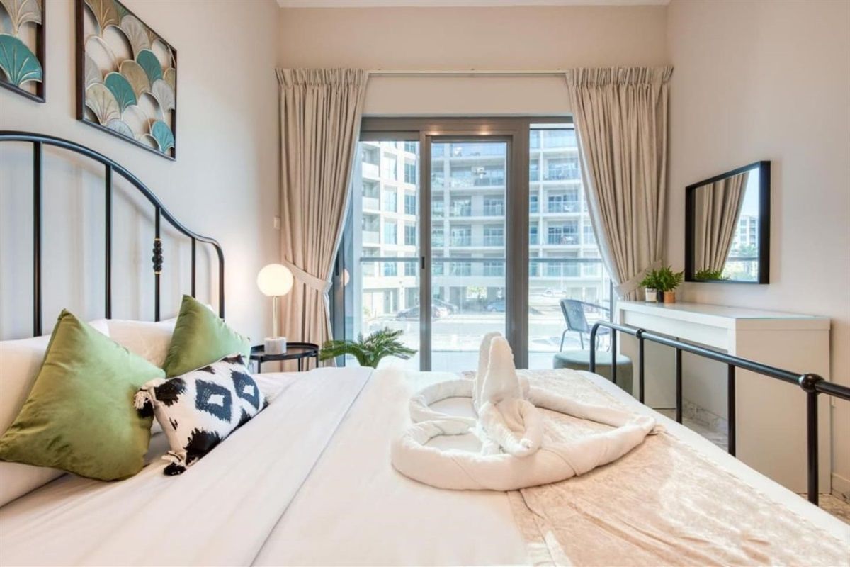 Quarto moderno com cama, escrivaninha e vista para a cidade através de amplas janelas.