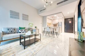 A modern living room with a sofa, coffee table, and dining area. - Stylish 1 BR + Pool & World Class Gym (Dubai)