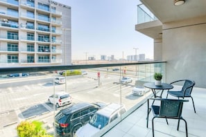 A balcony with a glass railing overlooking a parking area and a building. - Stylish 1 BR + Pool & World Class Gym (Dubai)