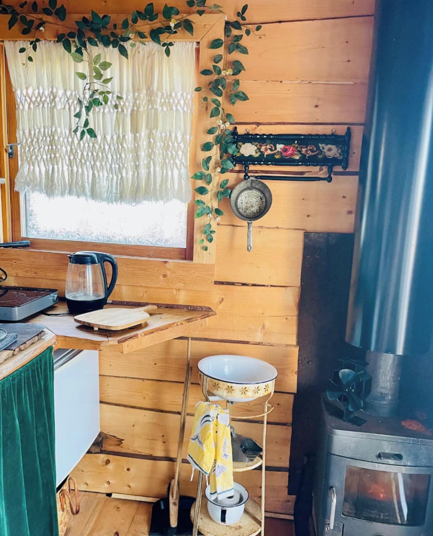 Una cucina rustica con pareti in legno, una finestra con tende, un fornello e diversi utensili da cucina.