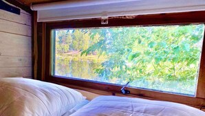 Una cama con sábanas blancas y una ventana con vista a follaje.