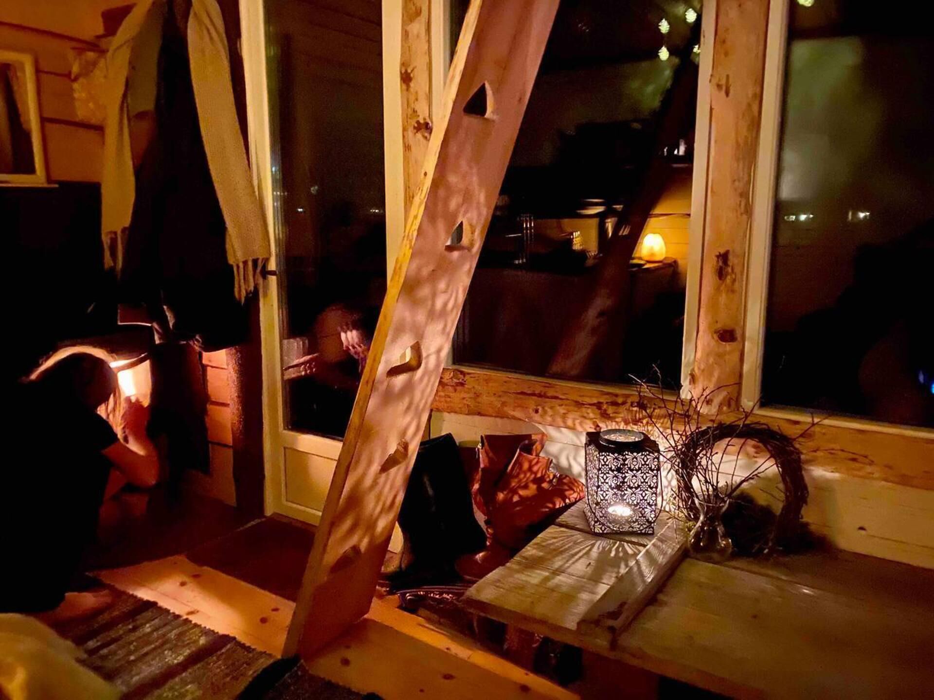 A cozy cabin interior with a wooden bench, a lantern, and a window overlooking a dimly lit area.