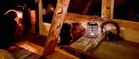 A cozy cabin interior with a wooden bench, a lantern, and a window overlooking a dimly lit area.