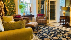 Ein gemütliches Wohnzimmer mit großem Fenster, einem gemusterten Teppich und einer Tür zu einem weiteren Raum.