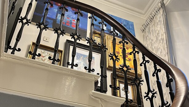 Eine Treppe mit aufwendigen schwarzen Metallgeländern und einer Holzhandläufe, die zu einem Raum mit einem Chandelier führt.