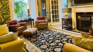 Ein Wohnzimmer mit Kamin, zwei Sesseln, einer Couch und einem großen Teppich mit Blumenmuster.