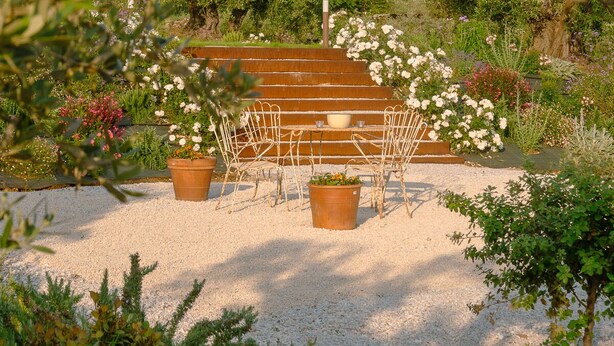 Ein Garten mit Sitzgelegenheit, inklusive Tisch und Stühlen, umgeben von verschiedenen Pflanzen und Blumen.