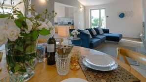 Ein modernes Wohnzimmer mit Essbereich, einer Küche im Hintergrund und einem großen Fenster, das für natürliches Licht sorgt.