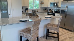 Una cocina moderna con armarios blancos, electrodomésticos de acero inoxidable y una isla central con taburetes de bar.