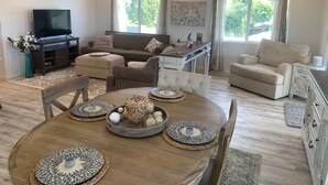 Un salón amplio con una gran mesa de comedor de madera, asientos cómodos, un televisor de pantalla plana y un ventilador de techo.