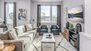 Un salon moderne avec un canapé, deux fauteuils, une table basse et un téléviseur posé sur un meuble.