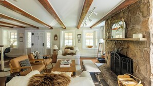 A cozy living room with a fireplace, wooden beams, and a stone wall. - Private Estate w/ Heated Pool, Pond & 10 Acres (Accord)