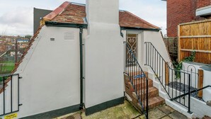 Una casa blanca con tejado de tejas rojas, una chimenea y una escalera que conduce a una puerta con reja de metal.