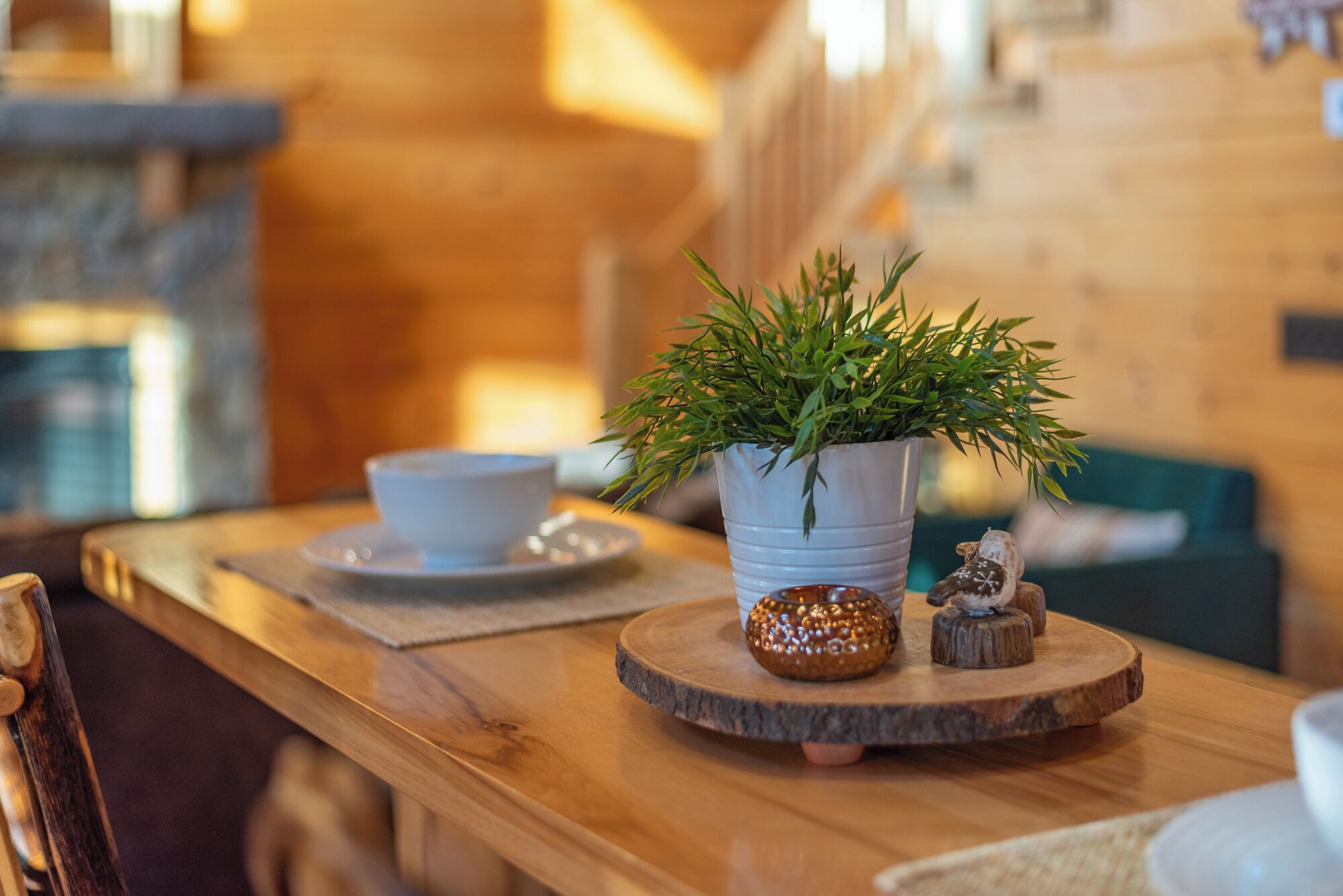 A wooden table with a white ceramic pot containing green foliage, a small decorative item, and a clear glass.