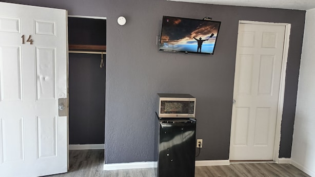 A room with a gray wall, a white door, and a television mounted above a microwave. - Napp Inn Motel (Rock Falls)