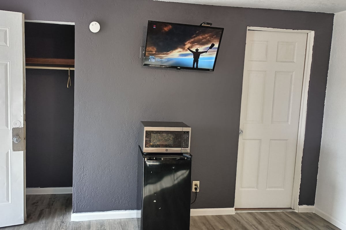 Una habitación con pared gris, puerta blanca y televisor sobre un microondas.