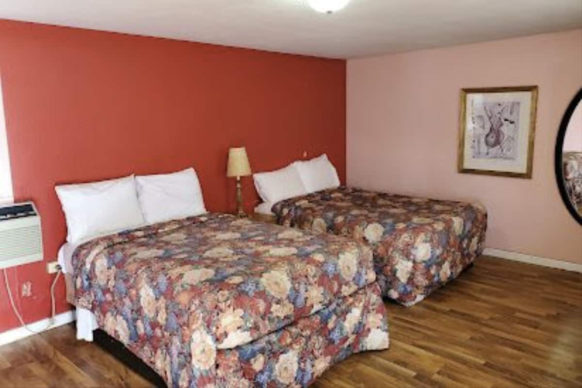 Una habitación con dos camas, una lámpara en el techo, un cuadro enmarcado en la pared y una ventana con persianas.