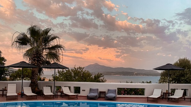 A poolside area with lounge chairs and umbrellas, overlooking a body of water and distant mountains. - Nisea Hotel Samos (Samos)