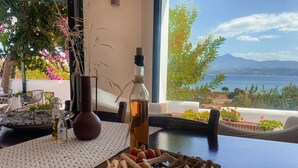 A table with a variety of snacks and a bottle of olive oil, set against a backdrop of a scenic view through a window. - Nisea Hotel Samos (Samos)