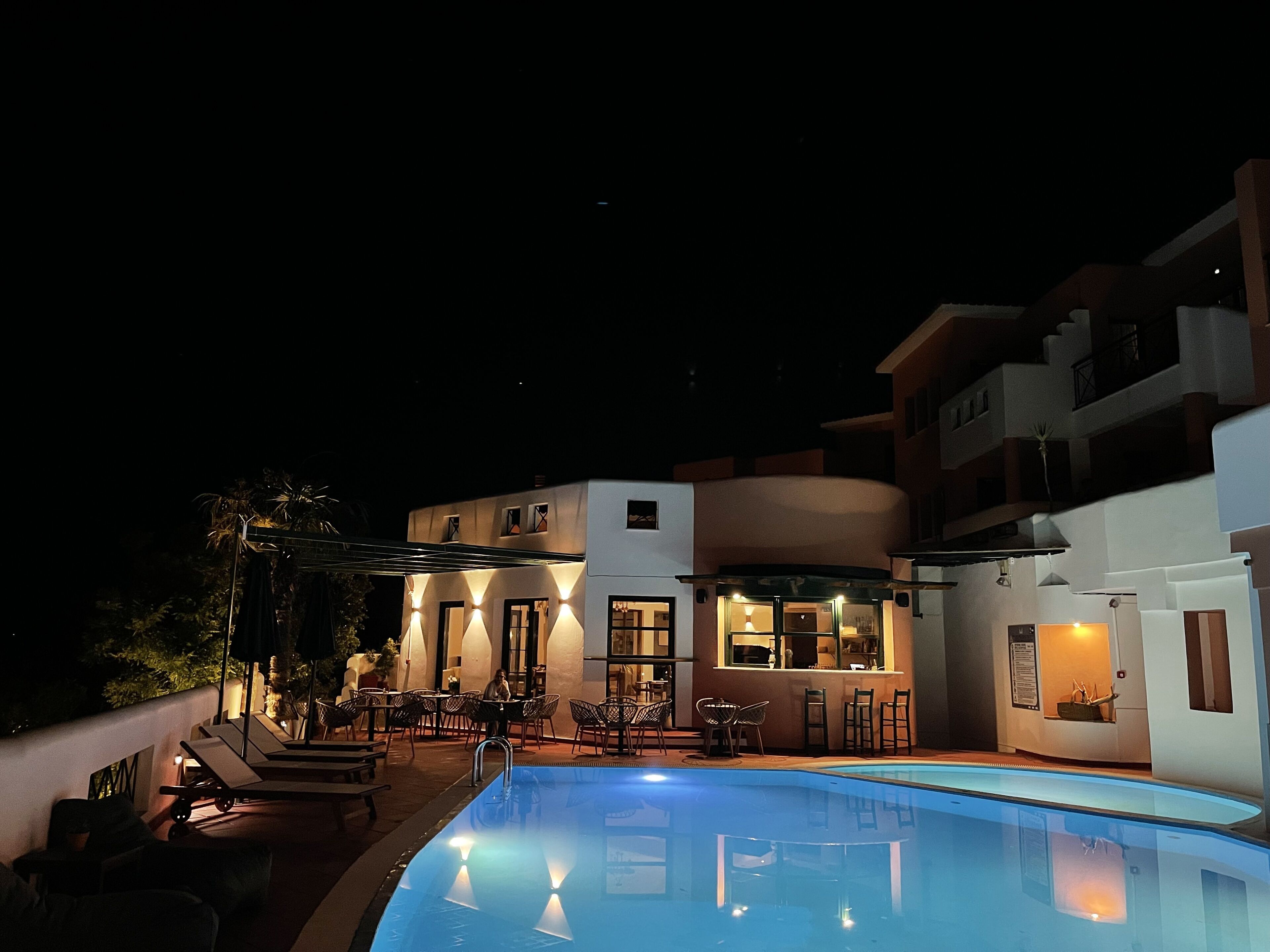 A nighttime view of a modern building with a swimming pool, outdoor seating, and a bar area.