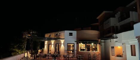 A nighttime view of a modern building with a swimming pool, outdoor seating, and a bar area.