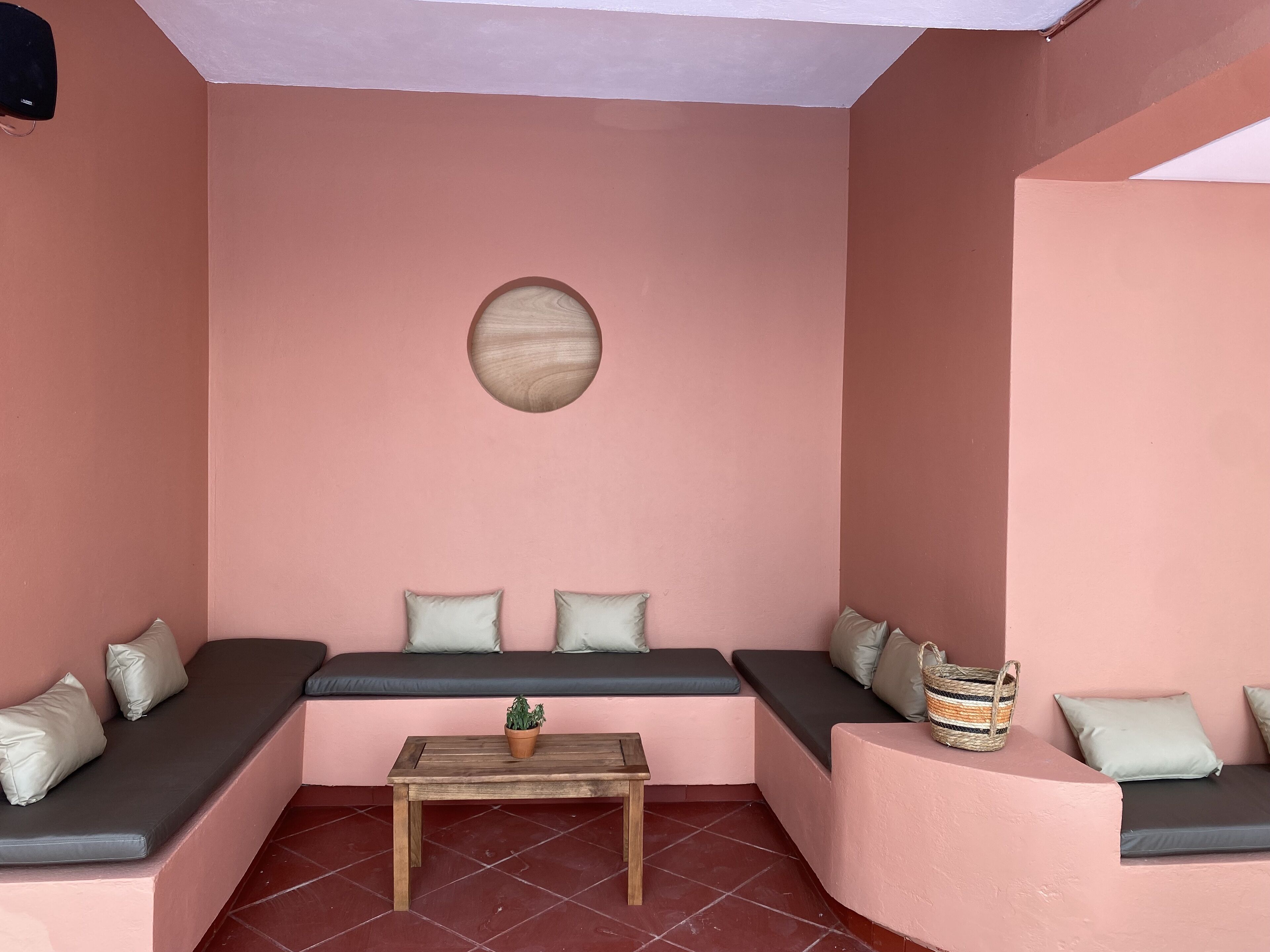 A cozy room with pink walls, a wooden table, and seating areas with cushions.