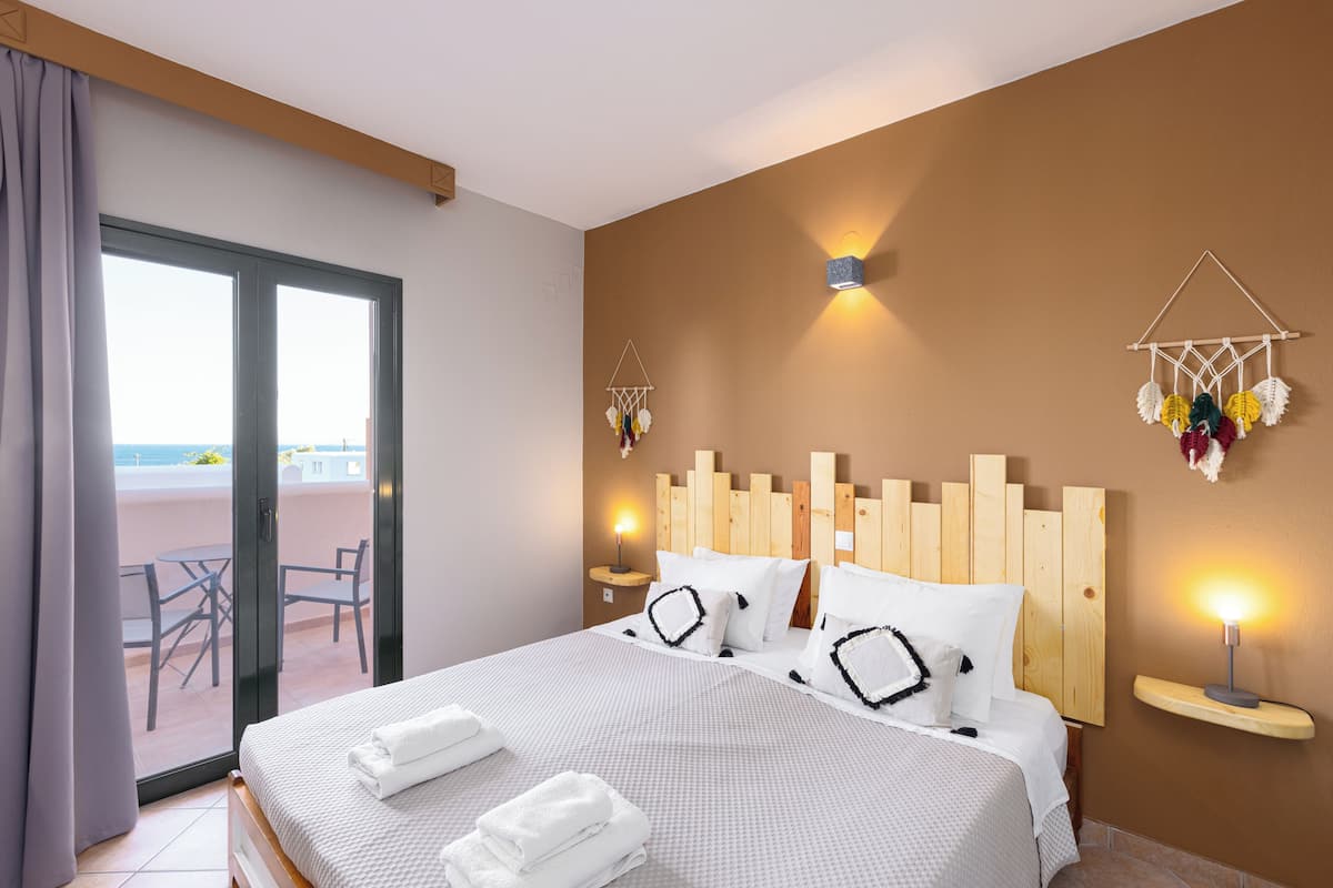 A hotel room with a large bed, a balcony with a table and chairs, and a wall-mounted dreamcatcher.