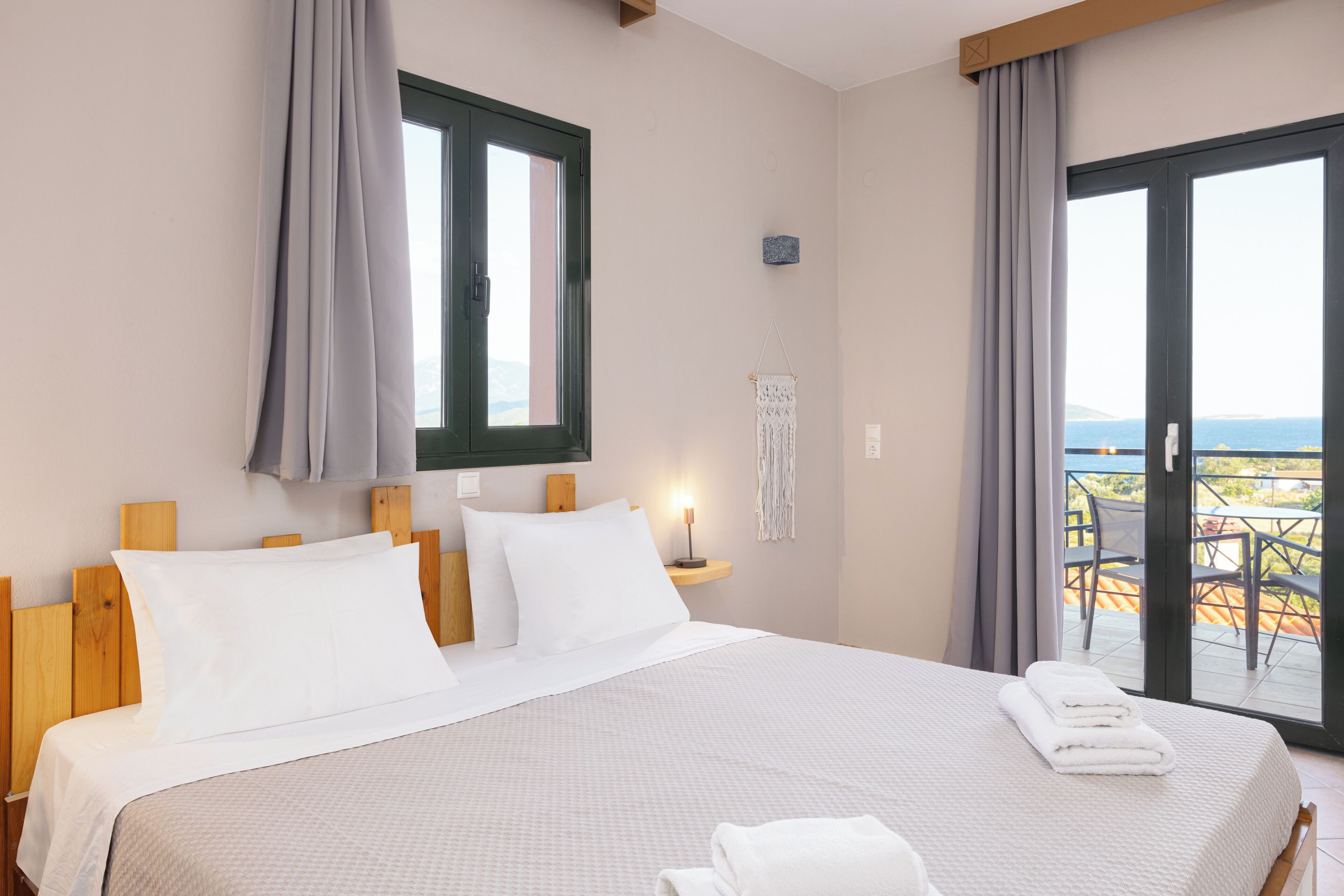 Un dormitorio con una cama grande, una ventana, un balcón con sillas y vistas al mar.