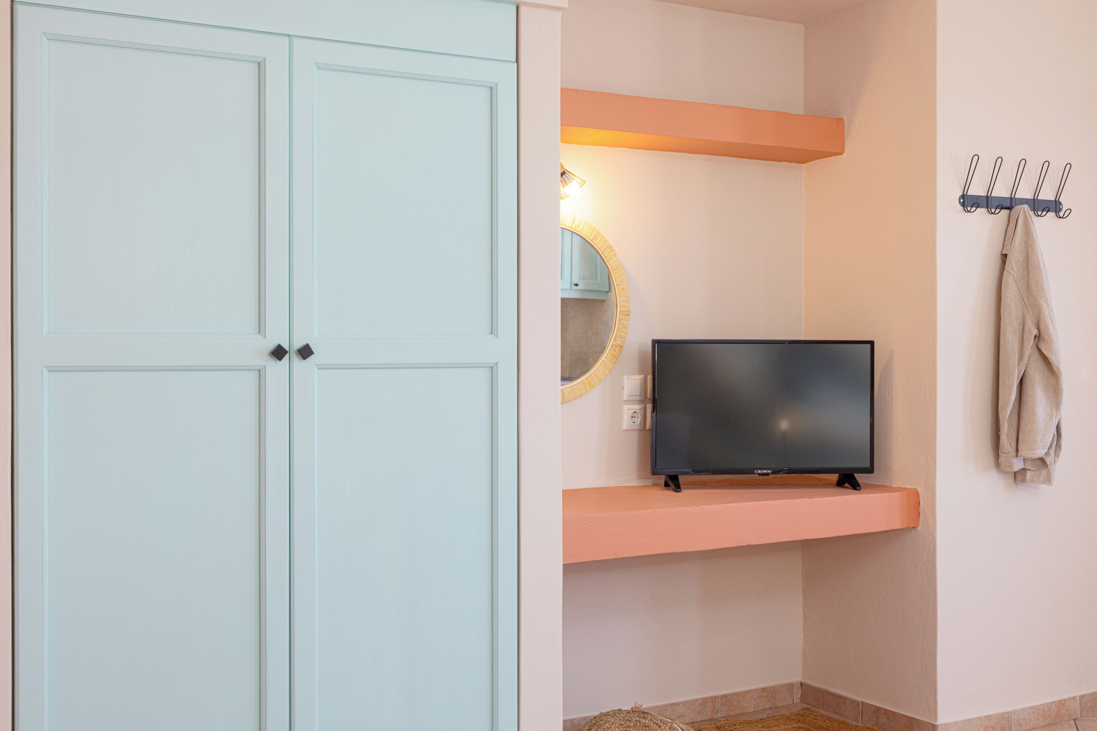 Un baño con un televisor en un estante, un perchero y un espejo con luz superior.