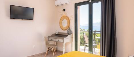 Un dormitorio con cama, escritorio, silla, televisor y balcón con vistas.