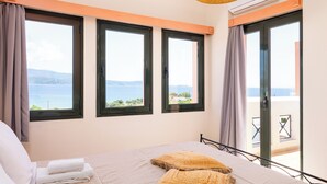 A bedroom with a bed, a view of the sea, and a balcony with a table and chairs. - Nisea Hotel Samos (Samos)