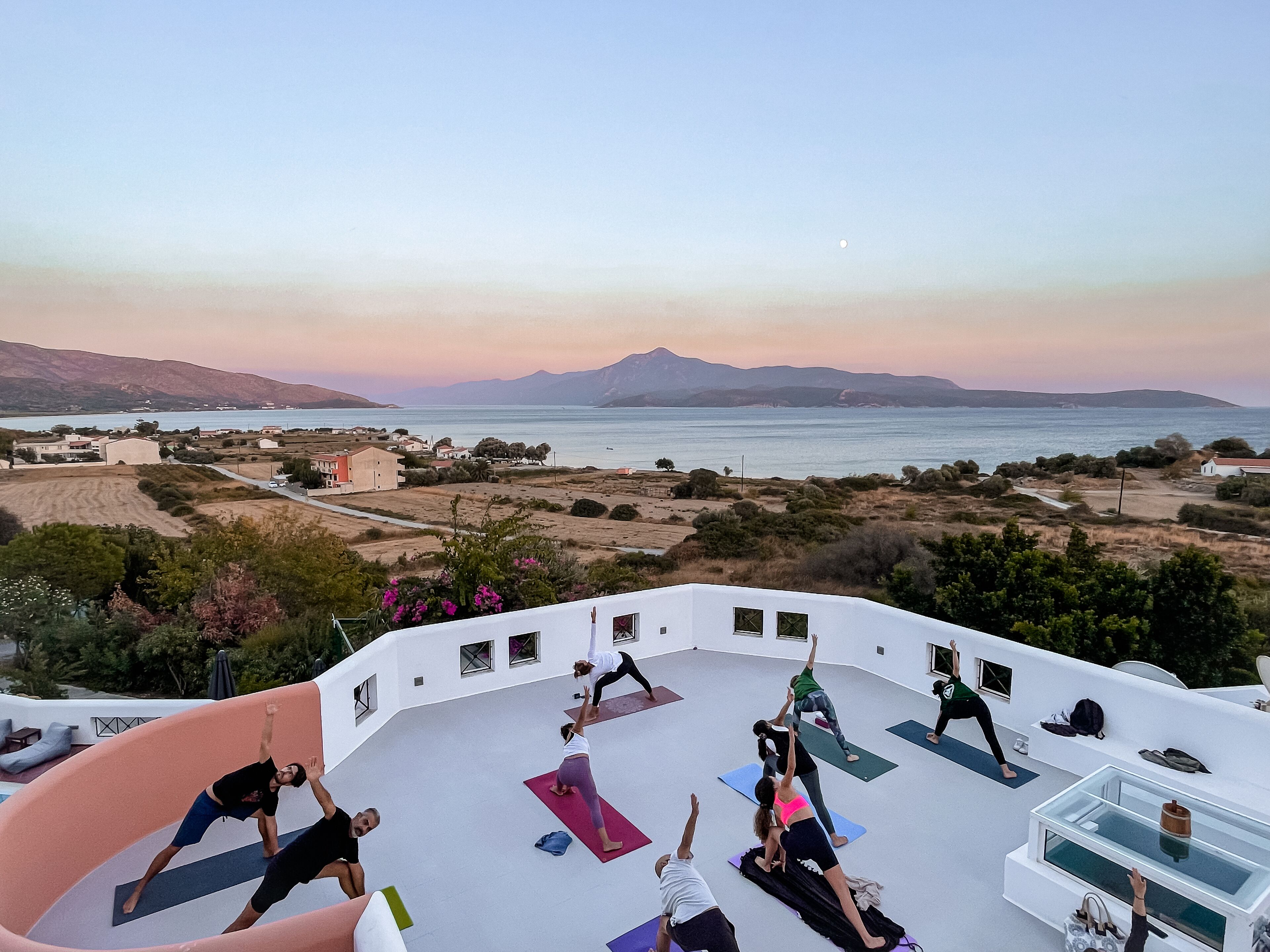 A group of people doing yoga on a rooftop with a scenic view of the sea and mountains.
