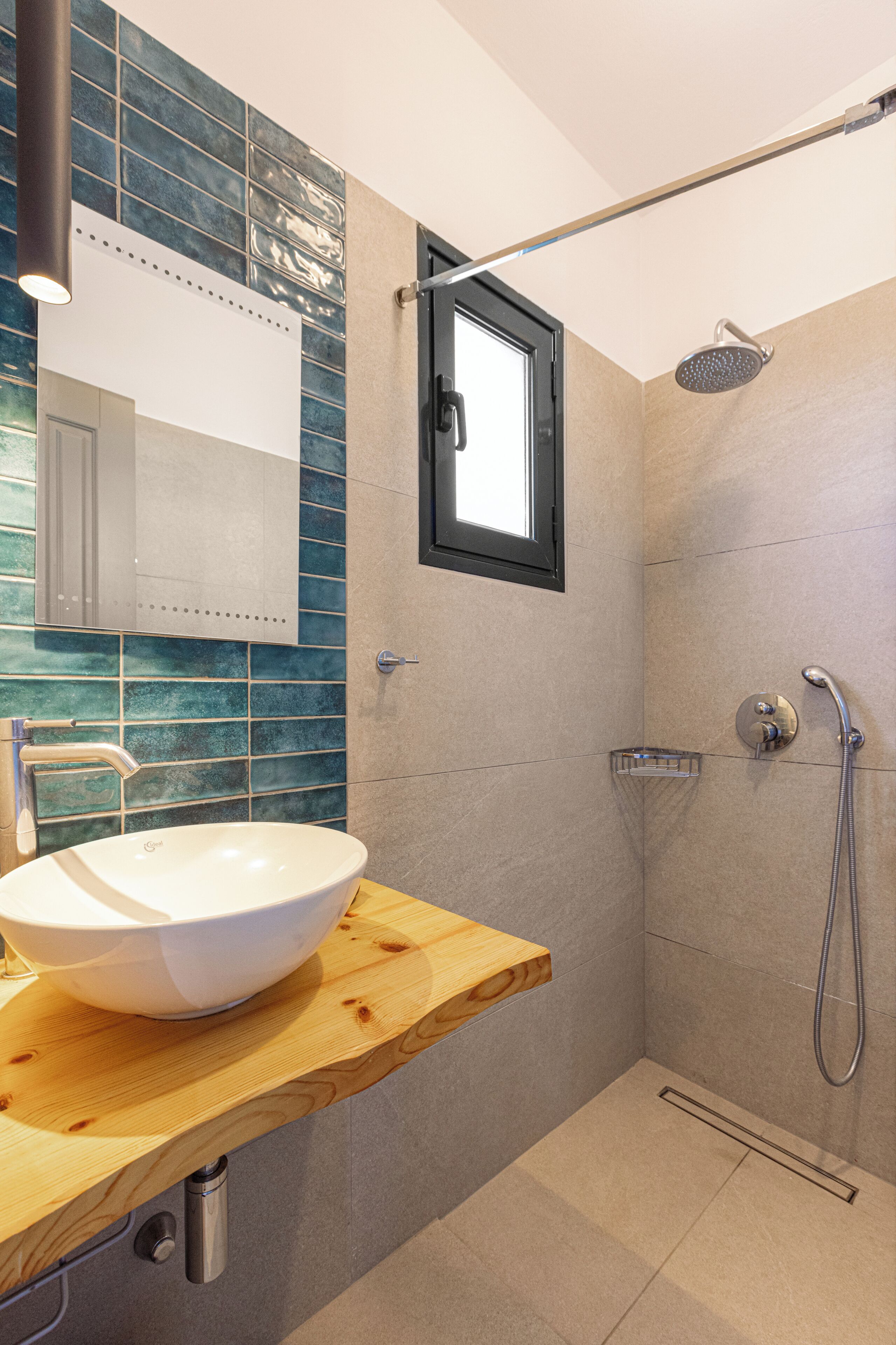 A modern bathroom with a white sink on a wooden countertop, a shower with a handheld showerhead, and a window above the shower.