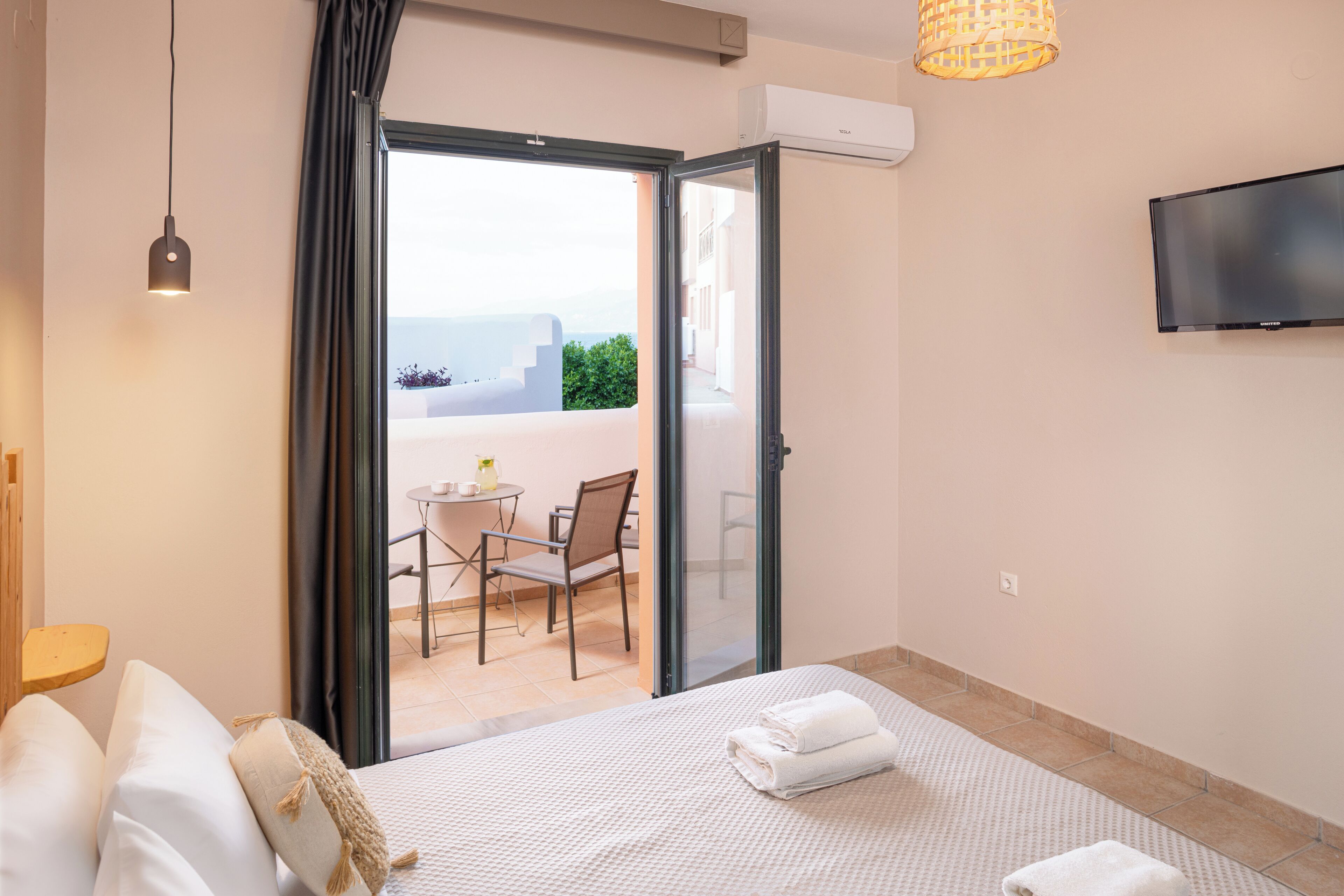A hotel room with a bed, a TV, a balcony with a table and chairs, and an air conditioning unit.