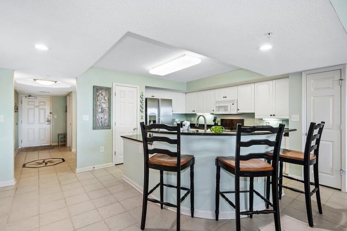 A modern kitchen with white cabinets, a central island with bar stools, and a dining area.