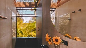 Un couloir étroit avec une grande fenêtre, un miroir et un vase rempli de tournesols.