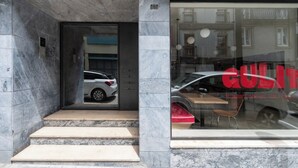 Ein Gebäudeeingang mit Glastür, ein geparktes Auto davor und die Hausnummer 240 an der Wand.