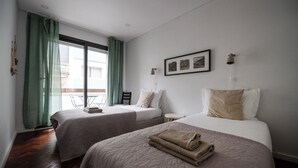Ein Hotelzimmer mit zwei Betten, einem kleinen Tisch, einem Stuhl, einem gerahmten Bild an der Wand und einem Balkon mit Aussicht.