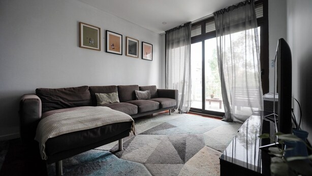 Ein modernes Wohnzimmer mit einer Couch, einem Flachbildfernseher und einem großen Fenster mit Vorhängen.