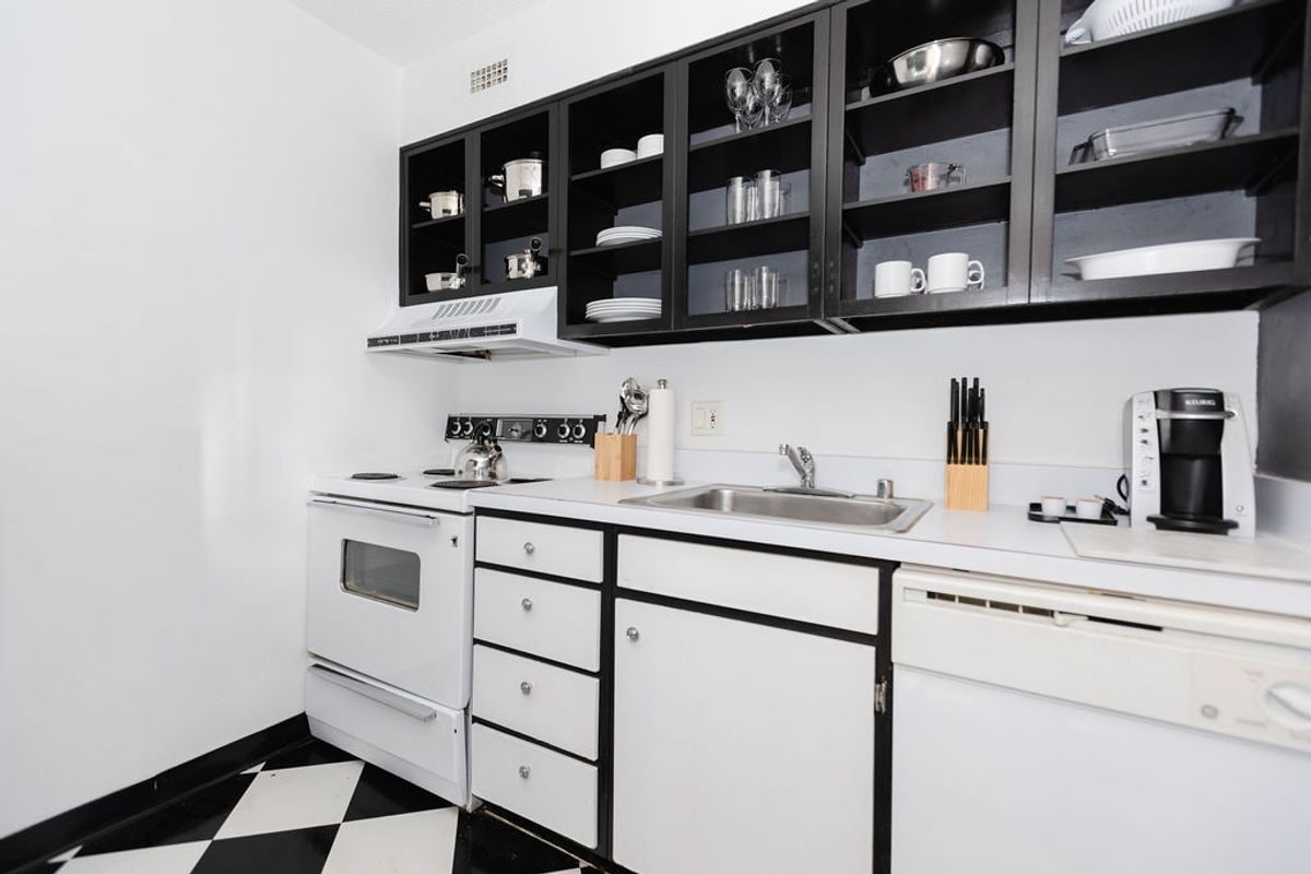 A kitchen with a black and white checkered floor, white cabinets, a stove, a sink, and a coffee maker.
