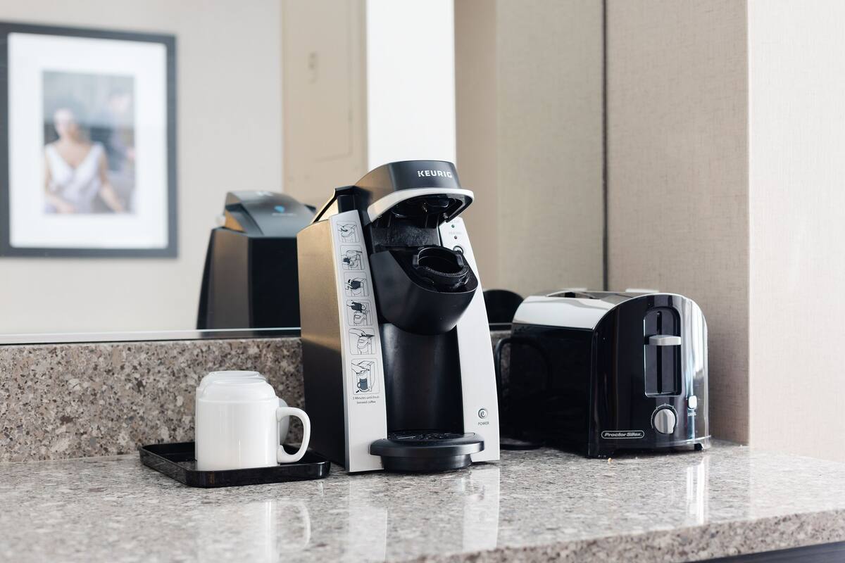 A coffee maker, a toaster, and a white mug on a kitchen counter.