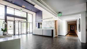 A modern hotel lobby with a reception desk, glass partitions, and a marble backsplash. - 2500 Penn, a Placemakr Experience (Washington)