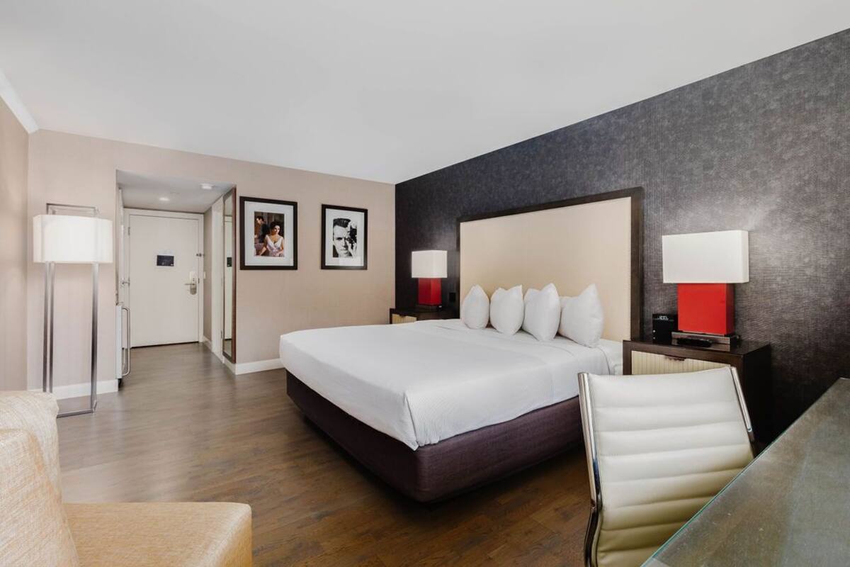 A modern hotel room with a large bed, bedside tables, a glass table, and a chair.