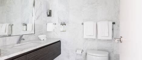 A modern bathroom with a marble sink, dark wooden vanity, white toilet, and a large mirror.